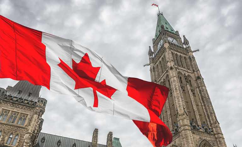 Canadian flag waving in front of the peace tower at parliament hill in ottawa, canada.