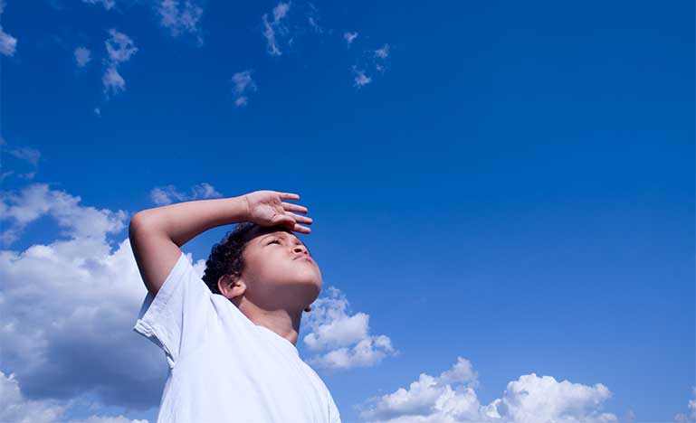 Close-up of a boy looking ahead against a blue sky