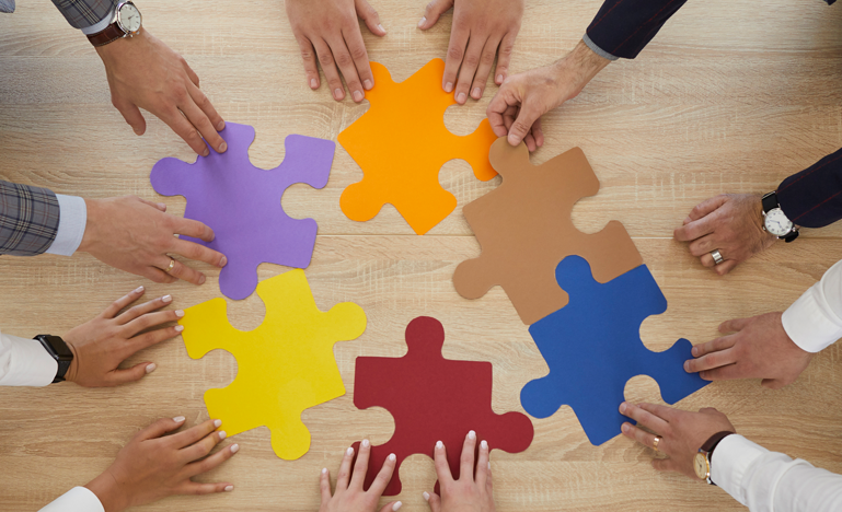 Teamwork in action: colleagues collaborate by putting together large puzzle pieces on a wooden table, symbolizing unity and collaboration in the workplace.