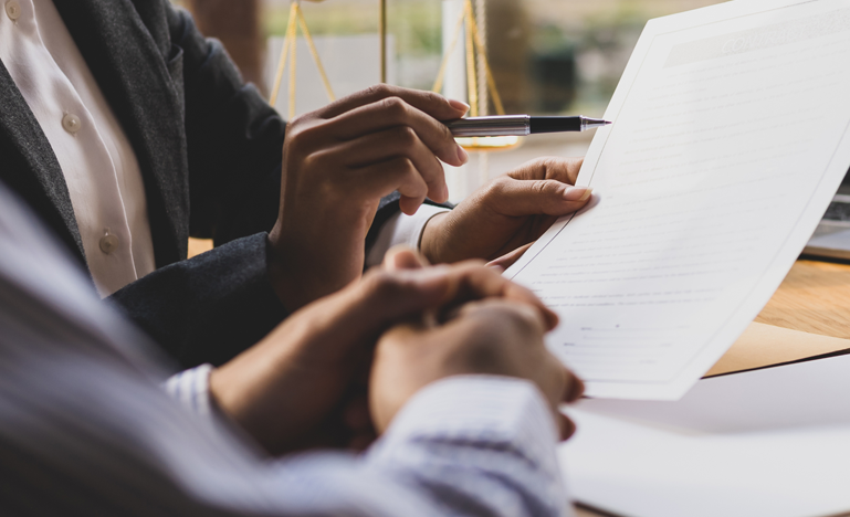 Two professionals reviewing and signing documents at a well-lit office table.