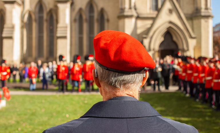 Veteran wearing a red beret watching a military ceremony outside a stone church.