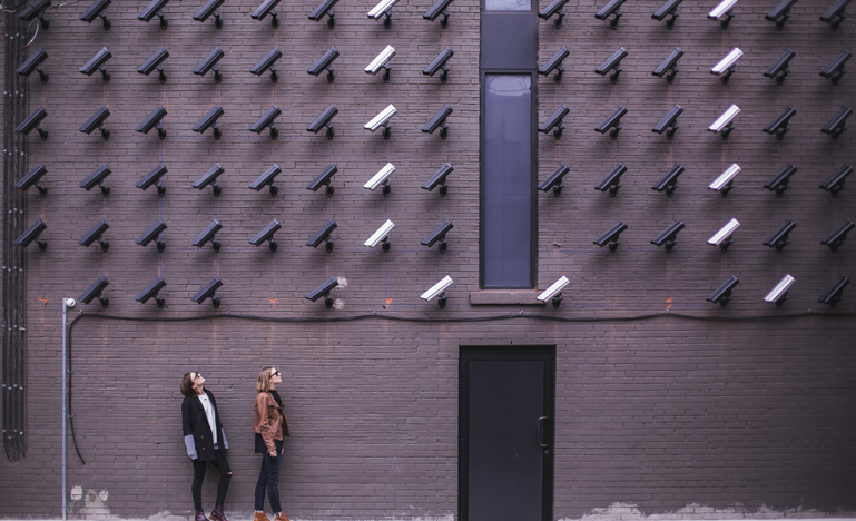 Two women facing security camerax above mounted on wall