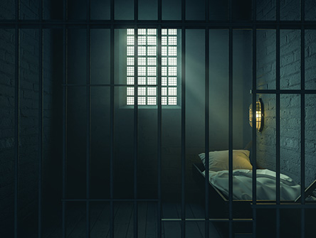 Dimly lit prison cell with metal bars and a small bed