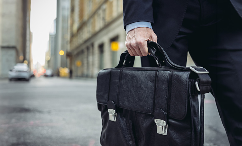 Walking in the middle of the street with his bag in his hand.