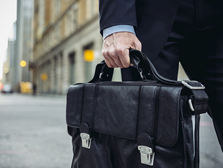 Walking in the middle of the street with his bag in his hand.