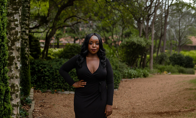 Woman in black dress standing in a garden path among trees.