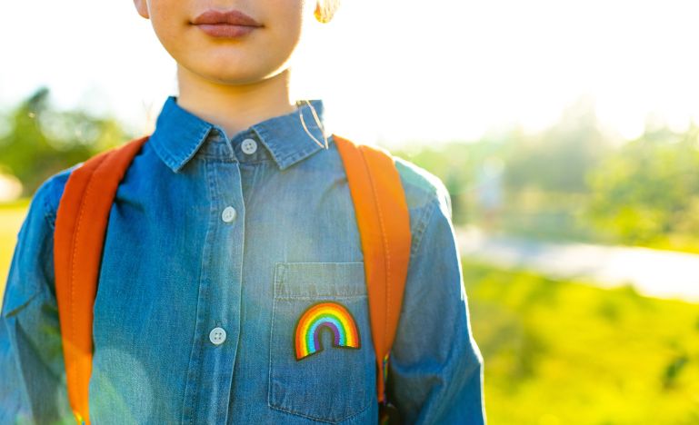 Child in a denim t-shirt with rainbow symbol wears a backpack in park