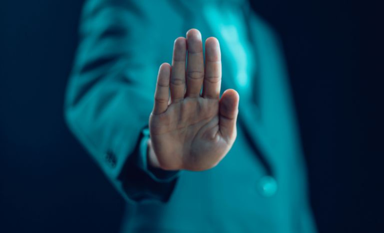 A person wearing a blue jacket holds up their hand to signal 'stop'