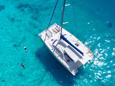 Aerial view of people snorkelling near a catamaran anchored in blue Caribbean water