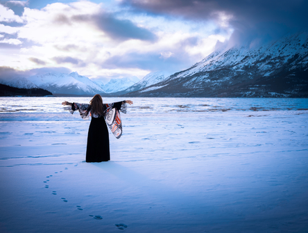 An Indigenous woman stands in the snow near a mountain lake