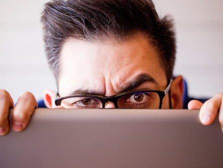 A man peeks over the top of laptop computer