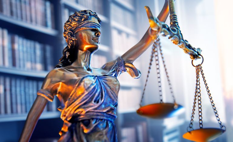 Lady justice stands in a law office with a bookshelf of law books in the background
